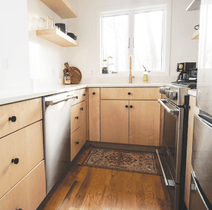 Galley kitchen with maple wood cabinetry, stainless steel appliances, open shelving, and a window providing natural light