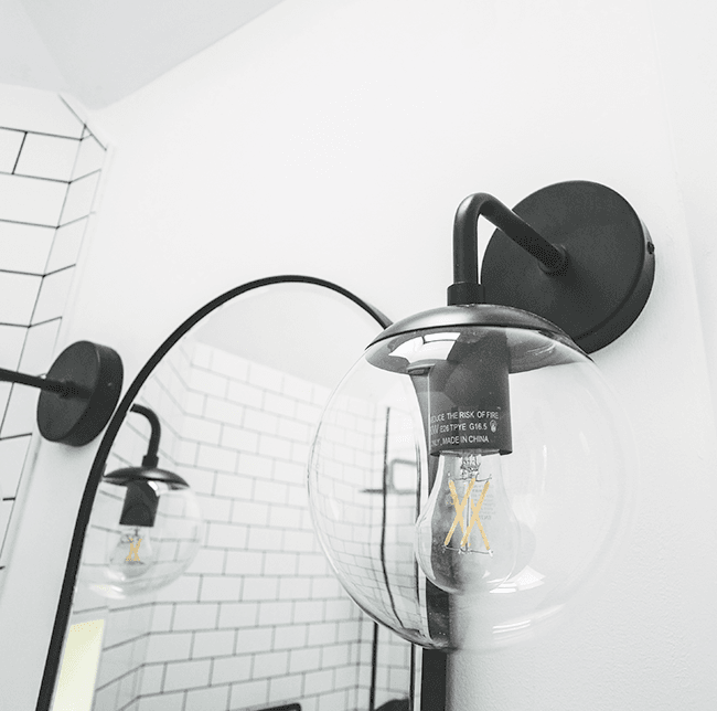 spherical incadescent bulb with black hardware against white wall