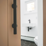 A modern, minimalist powder room with a floating white sink, black faucet, and hexagonal tile flooring.