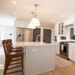 Modern kitchen with white cabinetry, island seating, pendant lights, and stainless steel appliances in a remodeled home