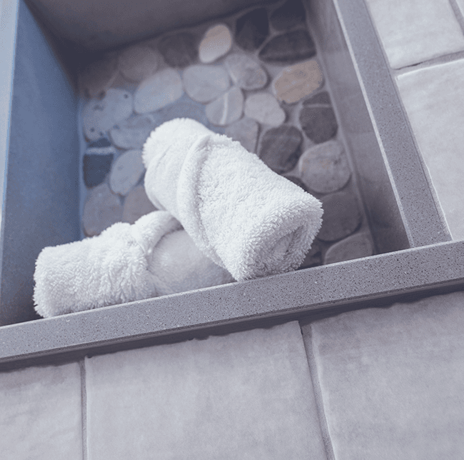 2 towels neatly rolled up on a bathroom shelf with stone details