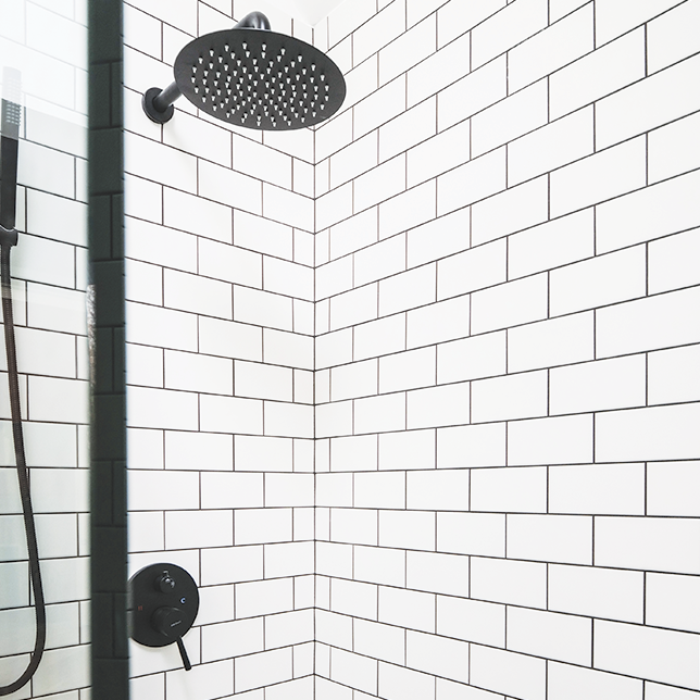 black showerhead and white tiles with black grout